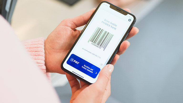 Payback Pay Eine Person hält ein Smartphone in der Hand. Darauf geöffnet ist die Payback-App mit der digitalen Karte.