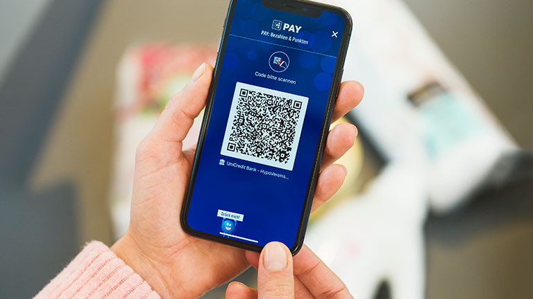 Payback Pay Eine Person hält ein Smartphone in der Hand. Darauf ist der QR-Code zum Bezahlen per Payback Pay zu sehen.