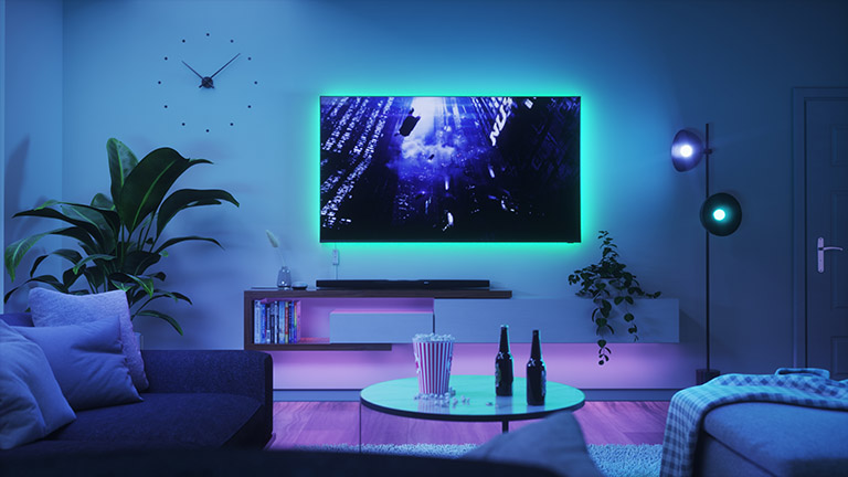 Nanoleaf Essentials Blick in ein Wohnzimmer. Hinter dem Fernseher leuchten Lightstrips von Nanoleaf.