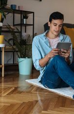 Eine Person sitzt auf einem Teppich und hält ein Tablet in der Hand.