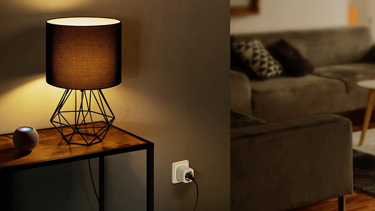 Ein Apple HomePod Mini auf einem Tisch. Daneben steht eine Lampe, die über eine Eve Energy mit dem Strom verbunden ist.