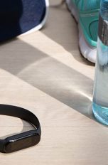 Das Fitness-Armband Mi Smart Band 5 von Xiaomi liegt auf einem hellen Holztisch. Ringsherum befinden sich Sportutensilien.