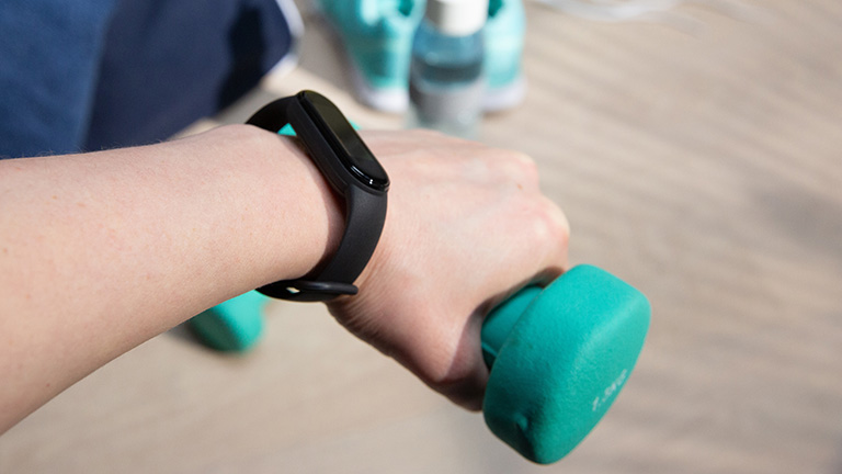Xiaomi MI Smart Band 5 Eine Hand ragt ins Bild und hält eine Hantel fest. Um das Gelenk schmiegt sich das Xiaomi Mi Smart Band 5.