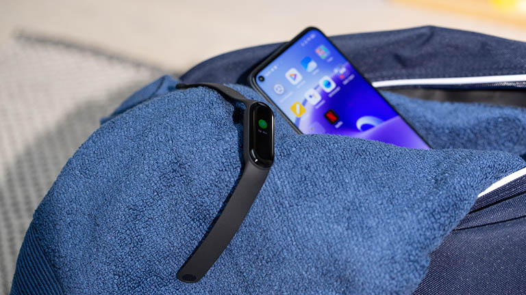 Xiaomi MI Smart Band 5 Das Xiaomi Mi Smart Band 5 liegt zusammen mit einem Smartphone auf einem blauen Handtuch, das halb aus einer Sporttasche herausragt.