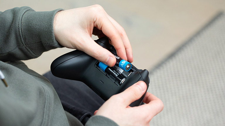 Microsoft Xbox Eine Person legt zwei Mignon-Batterien in den Controller der Xbox Series X ein.