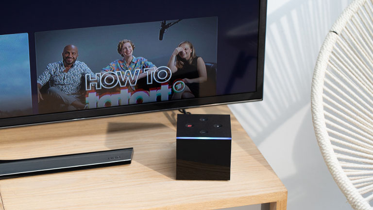 Amazon Fire TV Cube Der Fire TV Cube vor einem TV-Gerät. Der Lichtring leuchtet gerade blau.