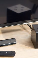 Der Amazon Fire TV Cube steht vor einem Fernseher. Daneben ist die Fernbedienung zu sehen.