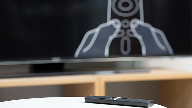 Mi TV Stick Auf dem TV ist der Einrichtungsbildschirm zum Xiaomi Mi TV Stick zu sehen. Davor liegt die Fernbedienung.