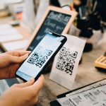 Eine Person hält ihr Smartphone auf einen QR-Code, um ihn mit der Kamera auszulesen.