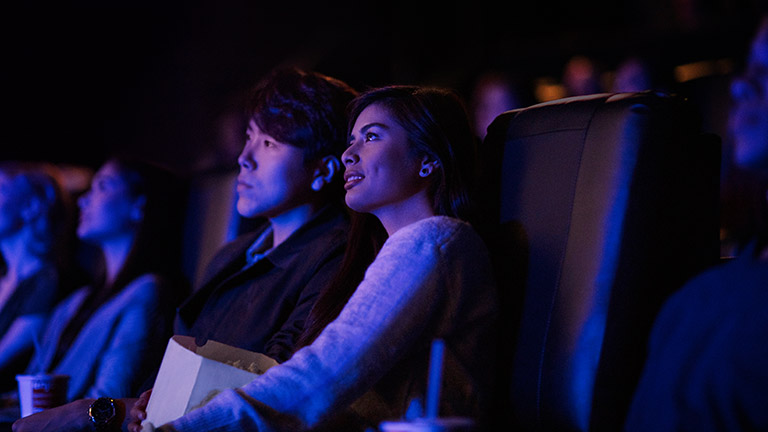 Dolby Atmos Zwei Personen sitzen in einem Kino und schauen einen Film.