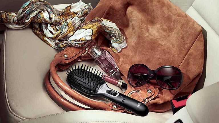 Braun Satin Hair 7 Die Satin Hair 7 Haarbürste von Braun liegt auf dem Beifahrersitz eines Autos neben einer Handtasche.