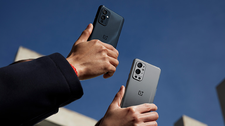 Zwei Hände halten das OnePlus 9 und das 9 Pro in die Luft. Zu sehen sind die Rückseiten der Smartphones.