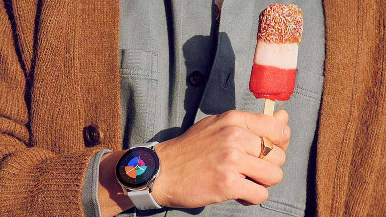 OnePlus Watch Eine Hand hält ein Stieleis. Am Gelenk sitzt die OnePlus Watch in Grau.