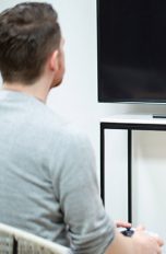 Eine Person sitzt vor einem Fernseher. Darunter steht eine PlayStation 5.
