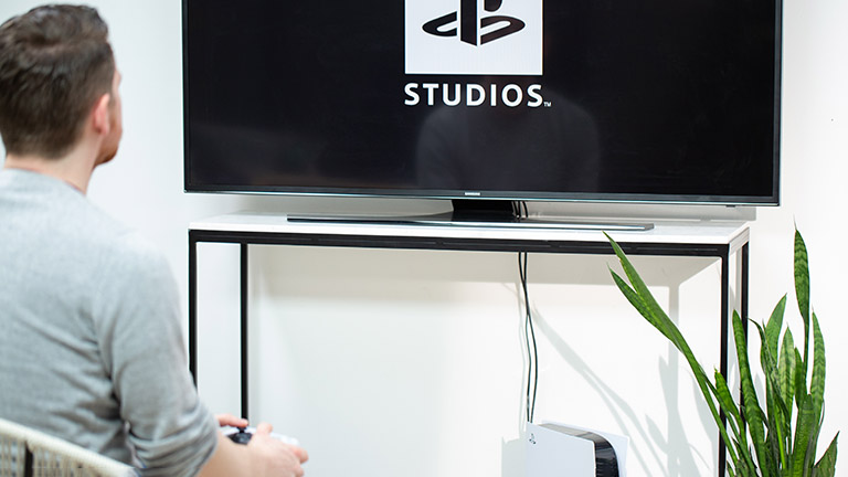 Eine Person sitzt vor einem Fernseher. Darunter steht eine PlayStation 5.