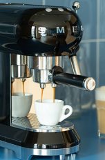 Eine Espressomaschine im Retro-Look der Marke Smeg steht auf einer Küchenzeile und bereitet einen Espresso zu.