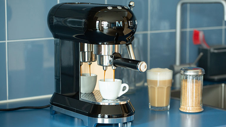 Eine Espressomaschine im Retro-Look der Marke Smeg steht auf einer Küchenzeile und bereitet einen Espresso zu.