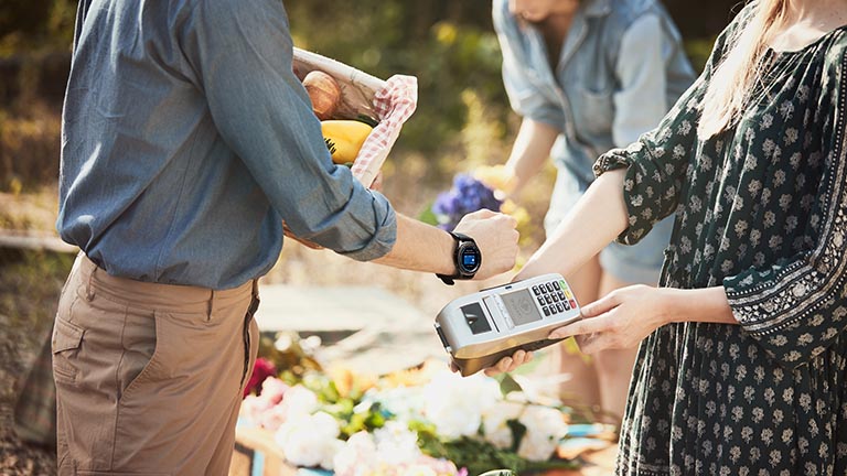 Samsung Pay Eine Person hält ihre Smartwatch am Handgelenk gegen ein Kartenlesegerät, um zu bezahlen.