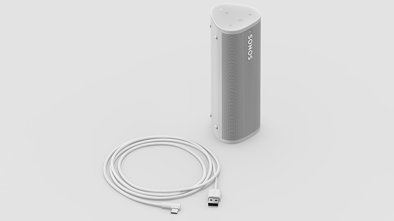 Sonos Roam Der Sonos Roam in weiß in aufrechter Position, daneben liegt das der Packung beiliegende Ladekabel.