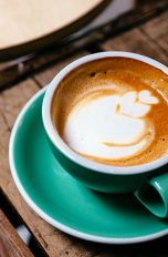 Foto einer Tasse gefüllt mit Kaffee, auf dem mit Milchschaum eine Blume angedeutet ist.