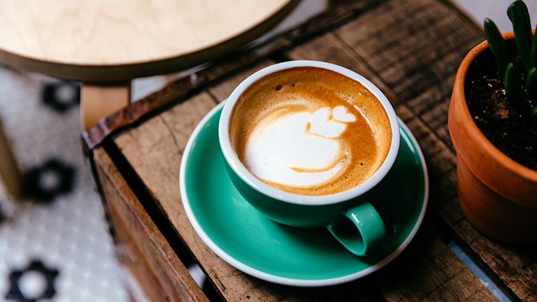 Foto einer Tasse gefüllt mit Kaffee, auf dem mit Milchschaum eine Blume angedeutet ist.