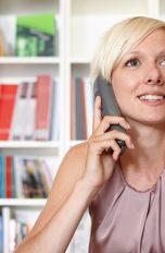 Eine Person sitzt an einem Schreibtisch und telefoniert mit einem Festnetztelefon.
