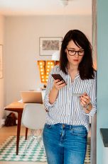 Eine Person steht an eine Wand gelehnt und hält ihr Smartphone in der Hand.