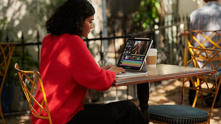 iPad Pro Eine Person sitzt an einem Kaffeetisch und bedient ihr iPad Pro über das Magic Keyboard.