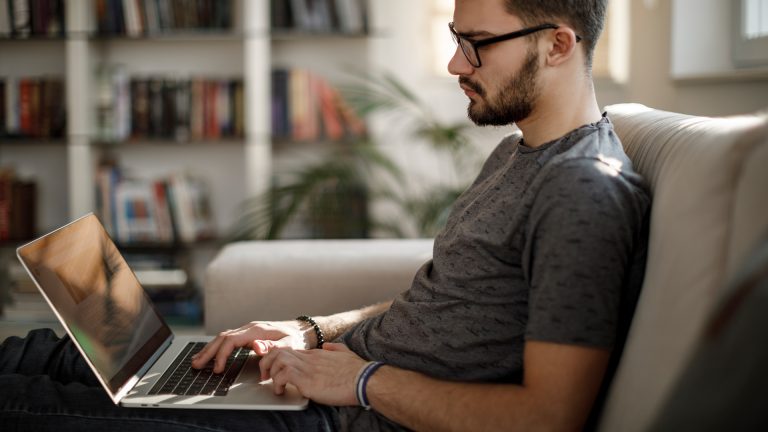 Gmail anmelden Eine Person sitzt auf dem Sofa und tippt auf einem Laptop herum.