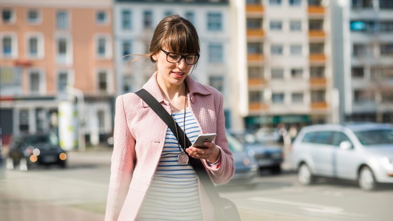 Gmail anmelden Eine Person geht durch die Stadt und schaut dabei auf ihr Smartphone.