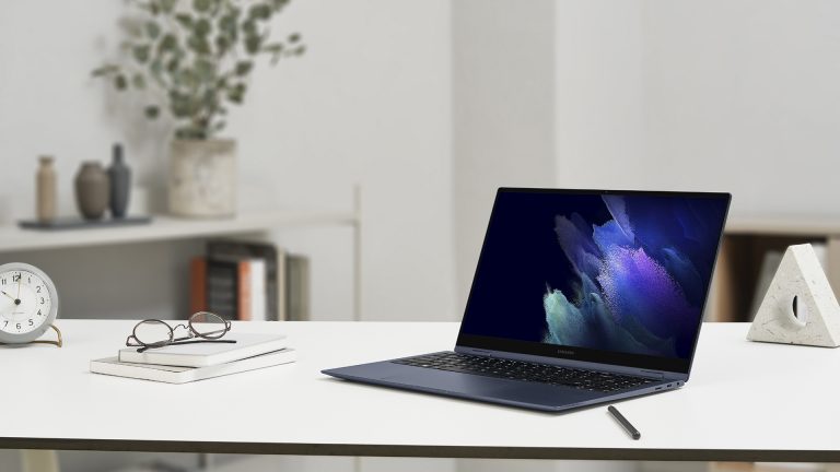 Ein aktuelles Galaxy Book Pro steht auf einem Tisch, daneben sind Notizblöcke und eine Brille zu sehen.