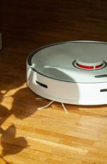 Ein Roborock S5 Max fährt über einen Holzboden auf eine Topfpflanze zu.