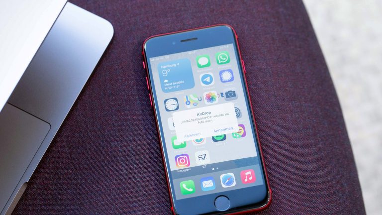 AirDrop Ein iPhone SE liegt auf einem Sessel und empfängt eine DAtei per AirDrop von einem MacBook Pro, das neben dem Smartphone liegt.