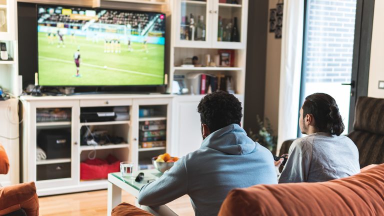 Fußball-EM 2021 Zwei Personen sitzen auf einem Sofa und schauen ein Fußballspiel im Fernsehen.