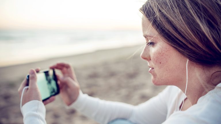 Fußball-EM 2021 Eine Person sitzt am Meer und schaut auf ihrem Smartphone einen Videostream.