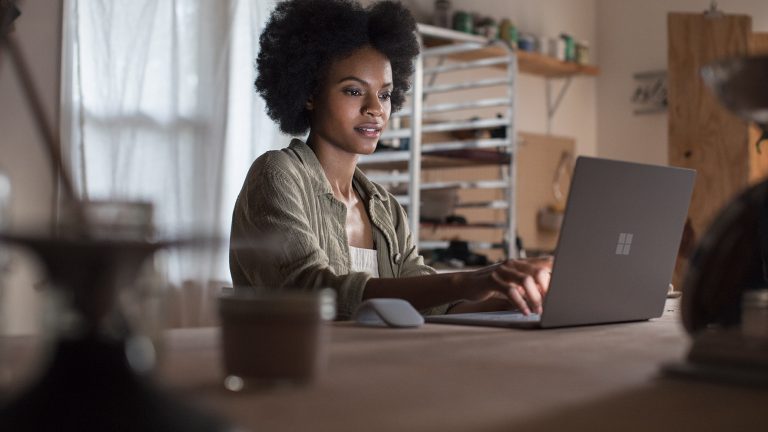 Microsoft Surface Arc Mouse Eine Person sitzt vor einem Surface-Laptop, daneben liegt die Funkmaus Surface Arc.