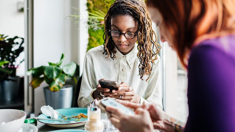 Nearby Share Zwei Personen sitzen an einem Esstisch und bedienen ihre Smartphones.