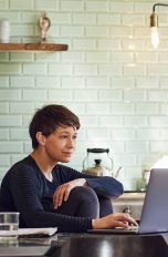 Eine Person sitzt an einem Esstisch und schaut auf einen Laptop.