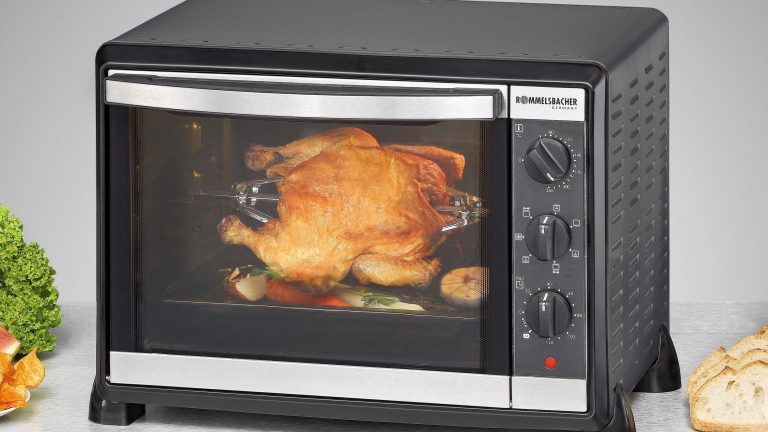 Rommelsbacher Minibackofen BG 1550 Ein Mini-Backofen mit einem ganzen Hänchen darin auf einer Küchenplatte.
