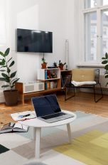 Blick in ein Wohnzimmer mit einem MacBook auf dem Couchtisch und einem Fernseher an der Wand.