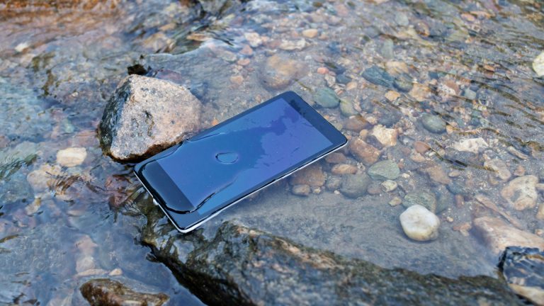 Ein Smartphone liegt in einem Bach. Es ist von Wasser bedeckt.