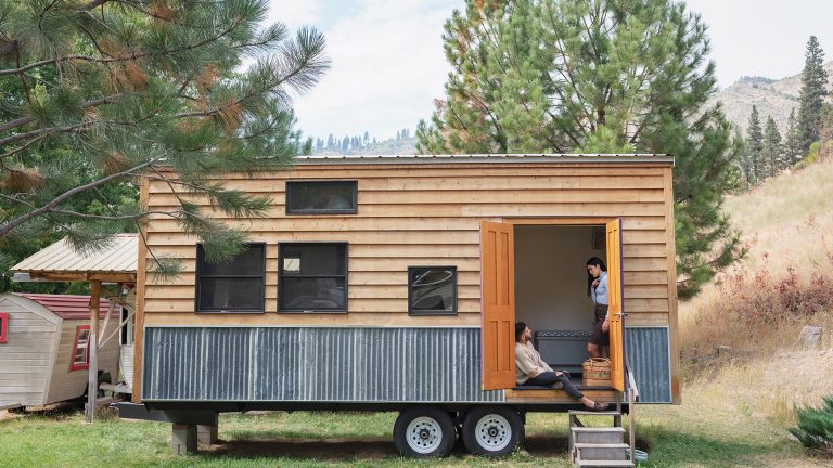 Tiny House Zwei Personen sitzen am Eingang eines Tiny House, das auf einen Anhänger gebaut ist.