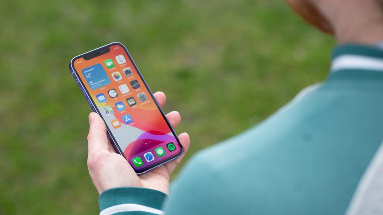 Eine Person hält ein iPhone 12 in der Hand und blickt darauf.