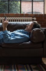 Eine Person liegt auf dem Sofa und hört mit Kopfhörern Musik vom Smartphone.