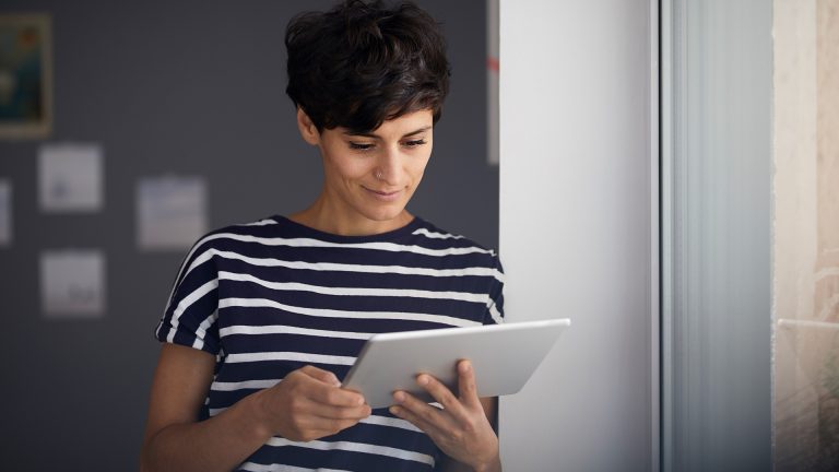Backup Eine Person lehnt an der Wand nahe eines Fensters und schaut auf ihr Tablet.