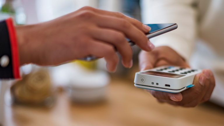 Backup Eine Person bezahlt mit ihrem Smartphone per NFC.