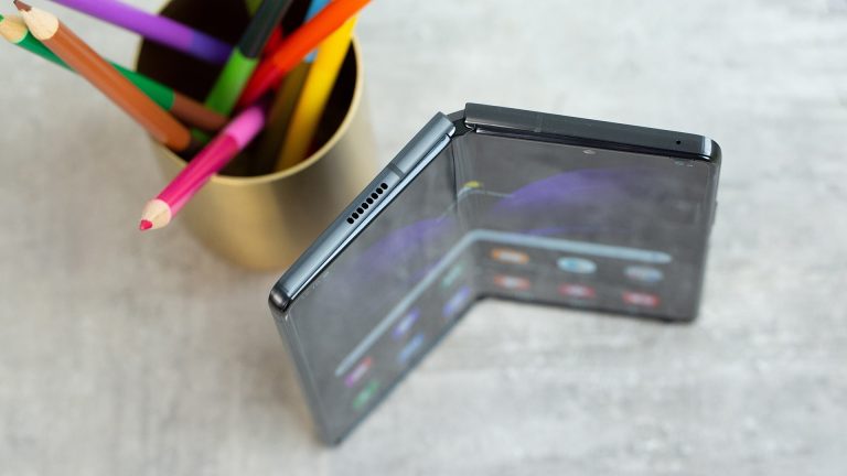Samsung Galaxy Z Fold 2 Draufsicht auf ein faltbares Smartphone, das auf einem Tisch steht, dahinter eine goldfarbene Dose mit Buntstiften.
