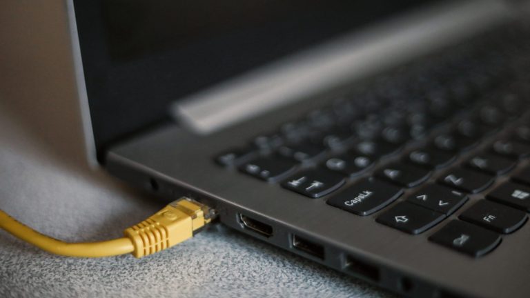 FritzBox einrichten Ein gelbes Netzwerkkabel steckt in einem aufgeklappten Laptop.