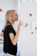 Eine Frau steht in einer Küche und schaut in einen geöffneten Kühlschrank.