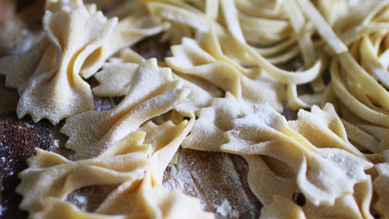 Lebensmittel selbstgemacht Aufnahme selbstgemachter Farfalle- und Linguine-Pasta, die auf einer bemehlten Fläche liegen.